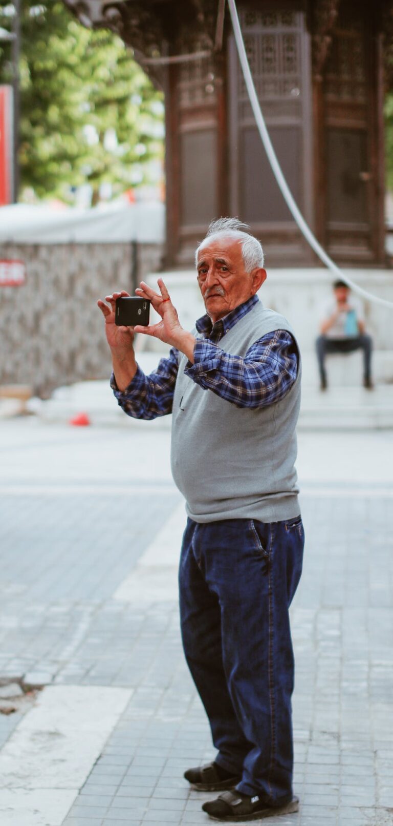 Senior man capturing city scenes with smartphone on a bustling street.